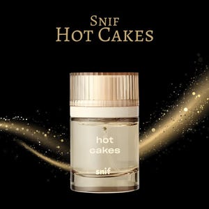K&ouml;nnte beinhalten: Ein Parf&uuml;mflakon mit goldener Kappe und einem transparenten Glask&ouml;rper. Auf der Flasche stehen die Worte "Hot Cakes" und "snif". Der Hintergrund ist schwarz mit goldenen Glitzerakzenten.