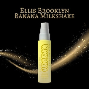 May include: A yellow spray bottle with a white top, labeled "Ellis Brooklyn Banana Milkshake." The bottle has the word "Banana" in a playful font. The background is black with gold glitter accents. The product is a hair and body fragrance mist.