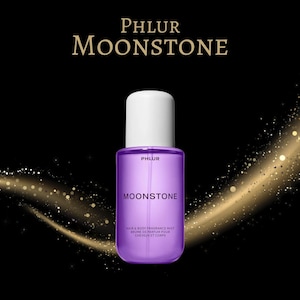 May include: A purple Moonstone hair and body fragrance mist bottle with a white cap. The bottle has the brand name "PHLUR" and the product name "MOONSTONE" printed on it. The background is black with gold sparkles.