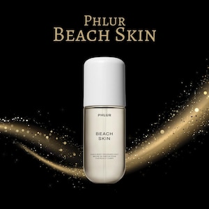 May include: A perfume bottle with a white cap and a clear body, labeled "PHLUR BEACH SKIN." The bottle is set against a black background with gold glitter accents. The text "Hair & Body Fragrance Mist" is also visible.