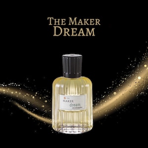May include: A clear glass bottle of The Maker Dream eau de parfum with a black cap and gold lettering. The bottle is sitting on a black background with a gold glitter effect.