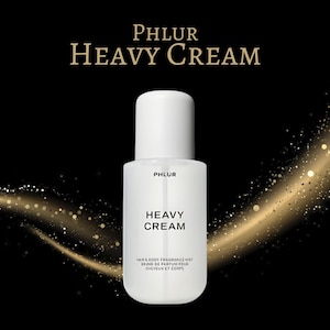 May include: A white bottle of PHLUR HEAVY CREAM hair and body fragrance mist. The bottle has a white cap and a white label with the product name in bold black letters. The background is black with gold sparkles.