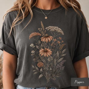 Woman wearing a Comfort Colors pressed flower shirt with a vintage botanical wildflower bouquet design, styled in a cozy cottagecore setting, perfect as a gardener gift, flower lover tee, or nature lover shirt.