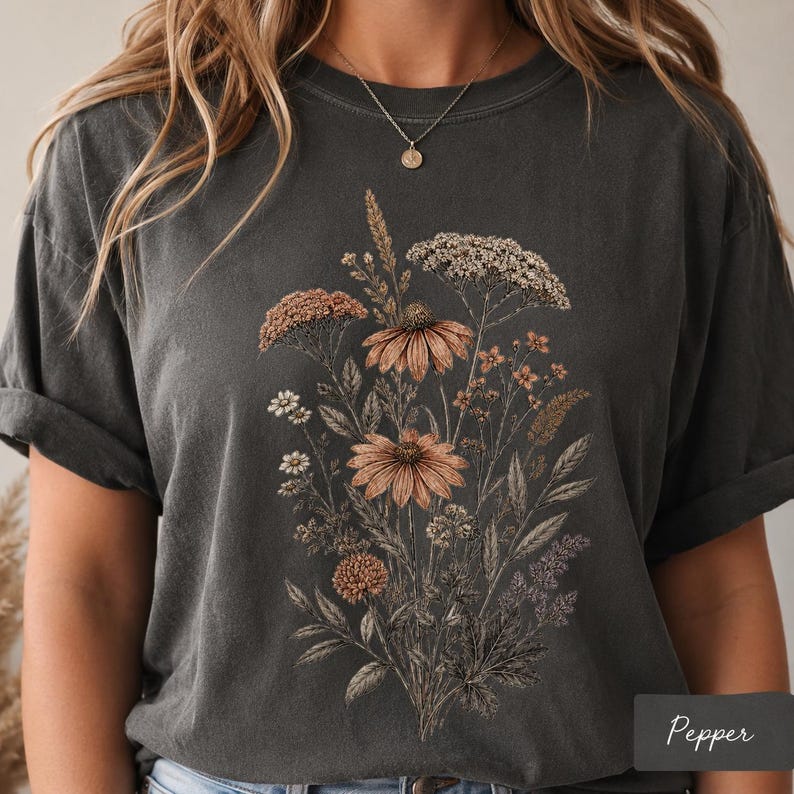 Woman wearing a Comfort Colors pressed flower shirt with a vintage botanical wildflower bouquet design, styled in a cozy cottagecore setting, perfect as a gardener gift, flower lover tee, or nature lover shirt.