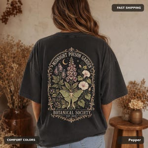 Woman wearing a Pepper Comfort Colors shirt with a large dark botanical poison garden and luna moth back print.
