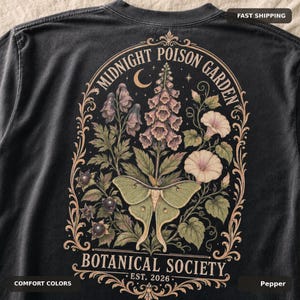 May include: A charcoal gray t-shirt featuring a back graphic of a pale green moth centered among botanical illustrations of foxgloves and morning glories, enclosed in an ornate frame with the text Midnight Poison Garden Botanical Society Est. 2026.