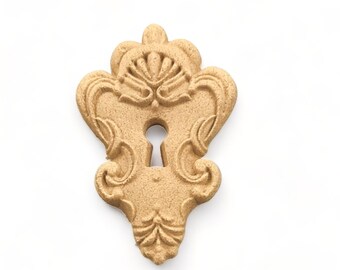 May include: A gold-colored keyhole shaped decorative piece with intricate details and a raised keyhole design.