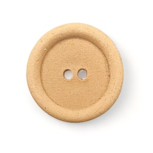 May include: A tan, round button with two holes. The button has a raised, circular rim around the edge and a slightly textured surface. The button is set against a white background.