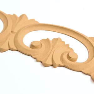 May include: A decorative wooden molding with a carved, ornate design. The molding is light brown and has a smooth, polished finish.