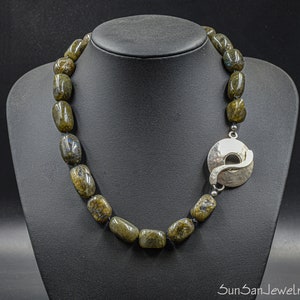 Può includere: Una collana realizzata con pietre di labradorite verde scuro con una chiusura in argento. La chiusura è un cerchio con un design curvo.