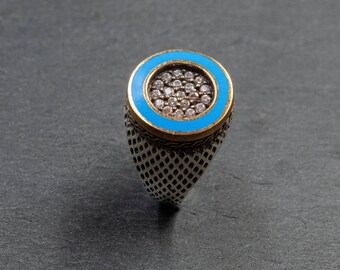 May include: A silver ring with a blue enamel band and a circle of small clear stones in the center.
