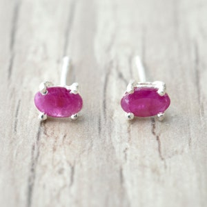 Może przedstawiać: Para srebrnych kolczyków z owalnymi, różowymi rubinami.