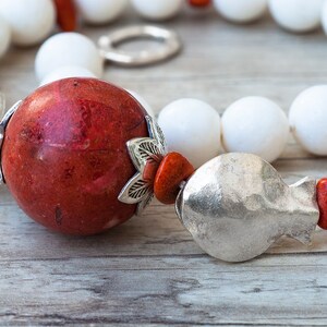 May include: A close-up of a red coral bead necklace with silver accents and white beads. The necklace is on a wooden surface.