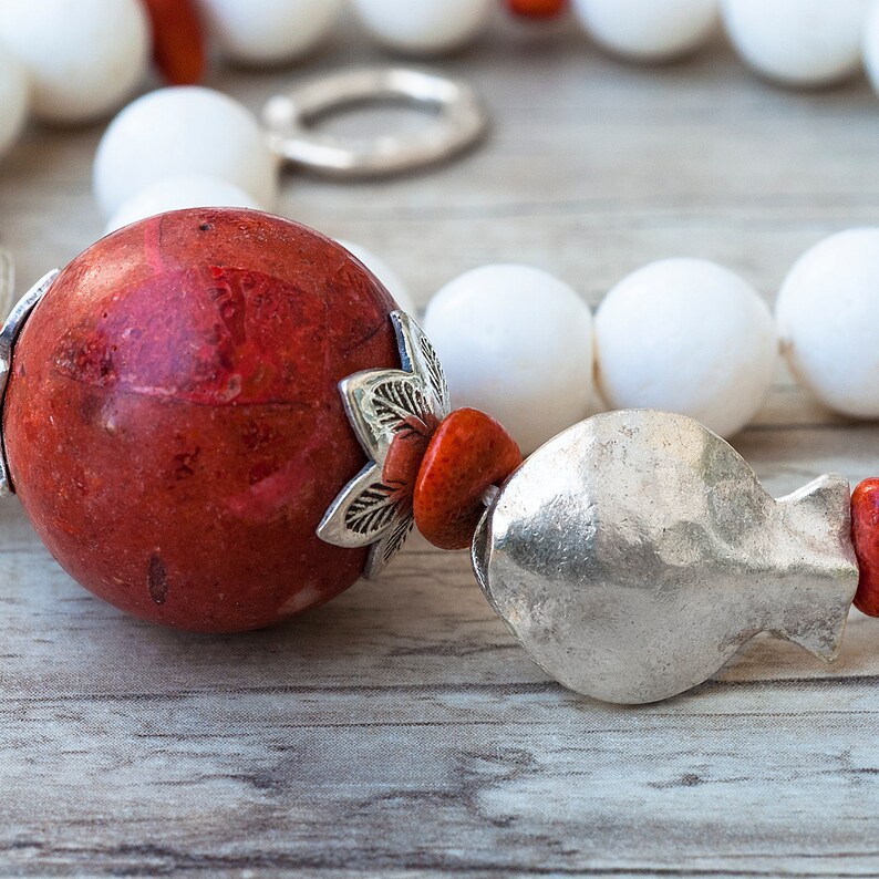 May include: A close-up of a red coral bead necklace with silver accents and white beads. The necklace is on a wooden surface.