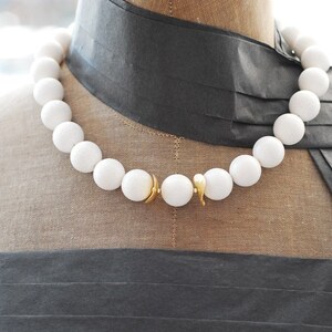 Puede incluir: Un collar de cuentas blancas con un cierre dorado. Las cuentas son grandes y redondas, y el collar est&aacute; en un maniqu&iacute;.