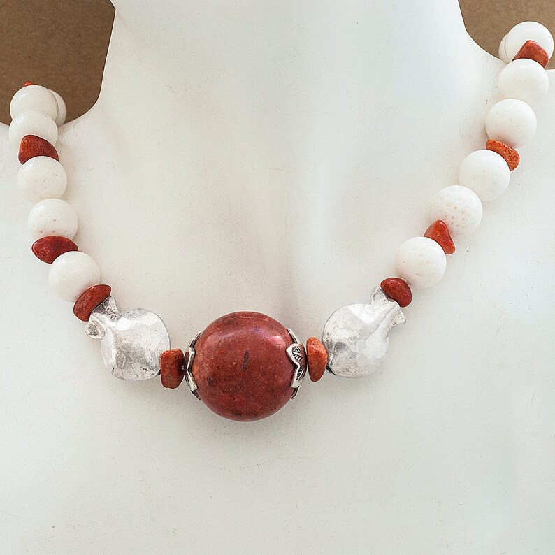 May include: A necklace with white and red coral beads and a large red coral pendant. The pendant is surrounded by silver accents.