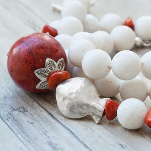 May include: A red coral bead with a silver charm and white coral beads on a string. The charm has a floral design.