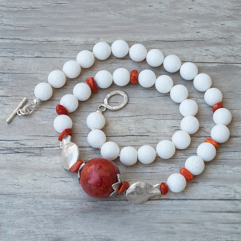 May include: A white coral bead necklace with a large red coral pendant and silver accents. The necklace has a toggle clasp.
