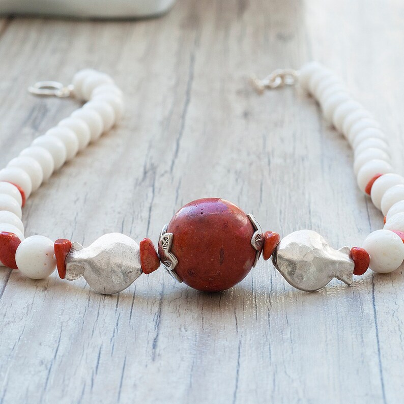 May include: A white and red beaded necklace with a large, round, red stone pendant and silver accents.
