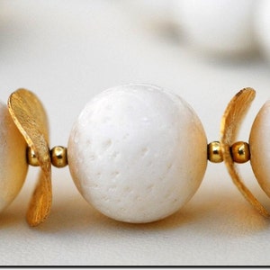 Puede incluir: Un collar de perlas blancas con detalles dorados. Las perlas son redondas y tienen una superficie texturizada. Los detalles dorados son peque&ntilde;os y delicados.