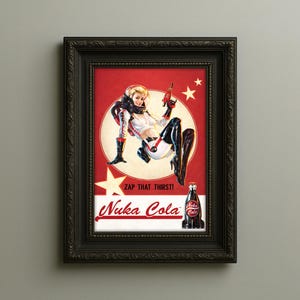 May include: Framed vintage-style poster with a retro advertisement for Nuka Cola. The artwork features a woman in a futuristic outfit, a bottle of cola, and the text "Zap That Thirst!" in a red and white color scheme.
