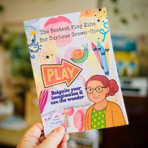 May include: A vibrant zine with the title "The Bestest Play Zine for Curious Grown-Ups". The cover art includes a snail, crayons, and a cartoon woman. The word "PLAY" is in a speech bubble.