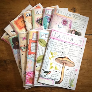 Könnte beinhalten: Ein Stapel von zwölf bunten Tagebüchern, jedes mit einem anderen Monat des Jahres auf dem Cover. Die Tagebücher sind mit handgezeichneten Illustrationen verziert, darunter Schmetterlinge, Blumen und Pilze. Der Text auf den Covern umfasst den Monat, das Jahr und einige interessante Fakten über jeden Monat.