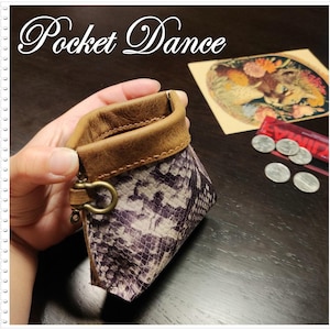 May include: A small, brown leather coin purse with a snake skin pattern. The purse has a metal clasp and a zipper. The purse is sitting on a wooden table.