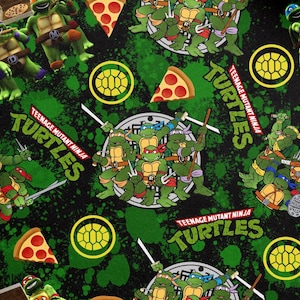 Op de afbeelding: Een herhalend patroon met de Teenage Mutant Ninja Turtles. Het ontwerp bevat groene schildpadden, pizzapunten en de woorden "Teenage Mutant Ninja Turtles" in groen en wit op een zwarte achtergrond met groene spetters.