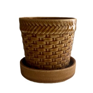 May include: A brown ceramic plant pot with a glossy finish and a textured basket-weave pattern on the exterior. The pot features a wide, flared rim with a braided design and sits securely inside a matching circular brown ceramic saucer base.