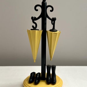 May include: A black metal umbrella stand with two yellow umbrellas and three pairs of black shoes. The stand has a yellow base.