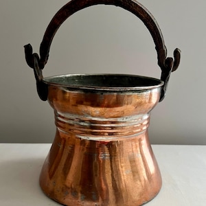 May include: A copper pot with a hammered finish and a wrought iron handle. The pot has a flared base and a rounded top.