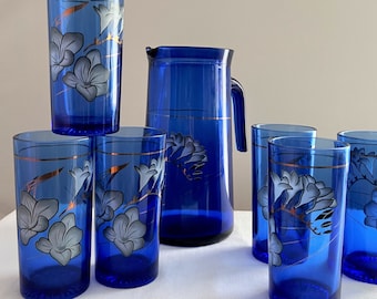 May include: A set of six cobalt blue glasses with gold trim and floral designs, and a matching cobalt blue pitcher with gold trim and floral designs.