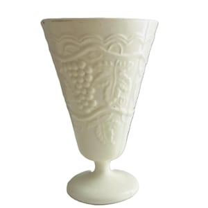 May include: Off-white, vintage-style goblet with a flared top and a pedestal base. The glass features a detailed embossed design of grapes and leaves, adding a classic touch. The goblet is likely made of glass and is suitable for serving beverages.