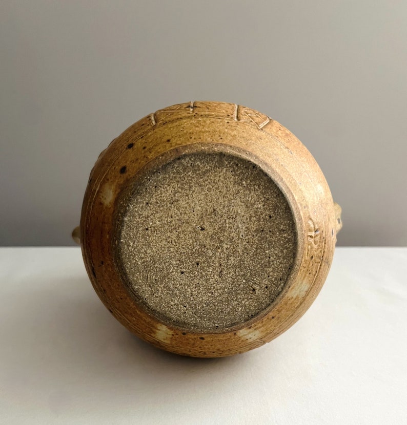 May include: A brown ceramic pitcher with a speckled glaze and a textured design. The pitcher has a wide base and a narrow spout.