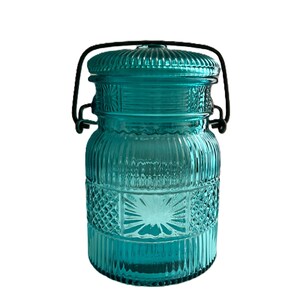 May include: A teal glass jar with a lid and a black metal handle. The jar has a ribbed design with diamond-shaped patterns. The lid is also teal and has a ribbed texture. The jar is likely used for storage or decoration.