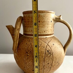 May include: A brown ceramic teapot with a textured surface and a carved design. The teapot is 7 inches tall.