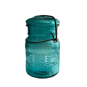 May include: A teal-colored glass jar with a lid and a metal clasp. The jar has a ribbed design on the lid and body, with a decorative pattern on the lower section. The jar is empty and sits against a white background.
