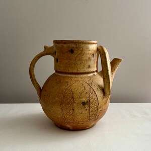 May include: A brown ceramic teapot with a unique design. The teapot has a rounded body with a spout and a handle. The handle is attached to the body with a small, decorative piece.