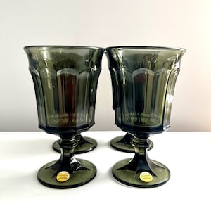 May include: Set of four dark green glass goblets with a fluted design and a round base. Each goblet has a gold sticker on the base that reads "Steubenville Oneida".