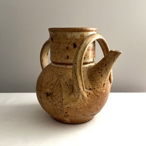 May include: A brown ceramic teapot with a unique design and two handles. The teapot has a speckled glaze and a slightly textured surface.