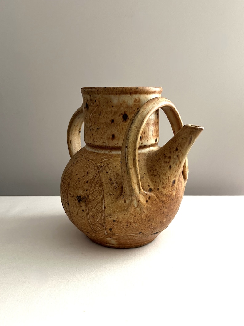 May include: A brown ceramic teapot with a unique design and two handles. The teapot has a speckled glaze and a slightly textured surface.