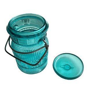 May include: A vintage-style, turquoise glass jar with a metal handle and lid. The jar has a ribbed design with embossed floral patterns. The lid is round with a ribbed pattern and a small handle. The jar is ideal for storage or decoration.
