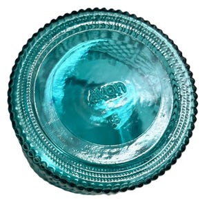 May include: A teal-colored glass bottle base with the embossed word "avon" and the number "5" visible. The base has a textured, ridged design around the edges.