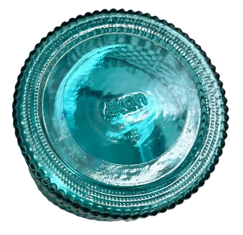 May include: A teal-colored glass bottle base with the embossed word "avon" and the number "5" visible. The base has a textured, ridged design around the edges.