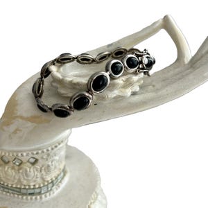 May include: A silver bracelet with black oval-shaped stones. The bracelet has a clasp closure.