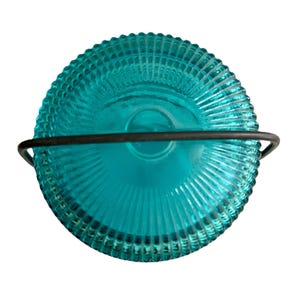 May include: A teal-colored glass candle holder with a ribbed design and a black metal handle. The candle holder is round and has a vintage aesthetic. The teal color is vibrant and eye-catching.