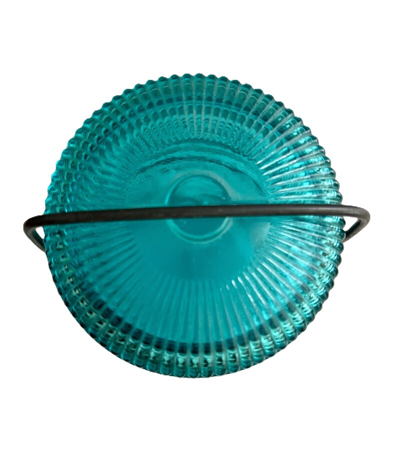 May include: A teal-colored glass candle holder with a ribbed design and a black metal handle. The candle holder is round and has a vintage aesthetic. The teal color is vibrant and eye-catching.