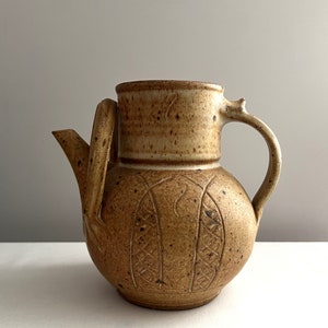 May include: A brown ceramic teapot with a textured surface and a carved design. The teapot has a handle and a spout.