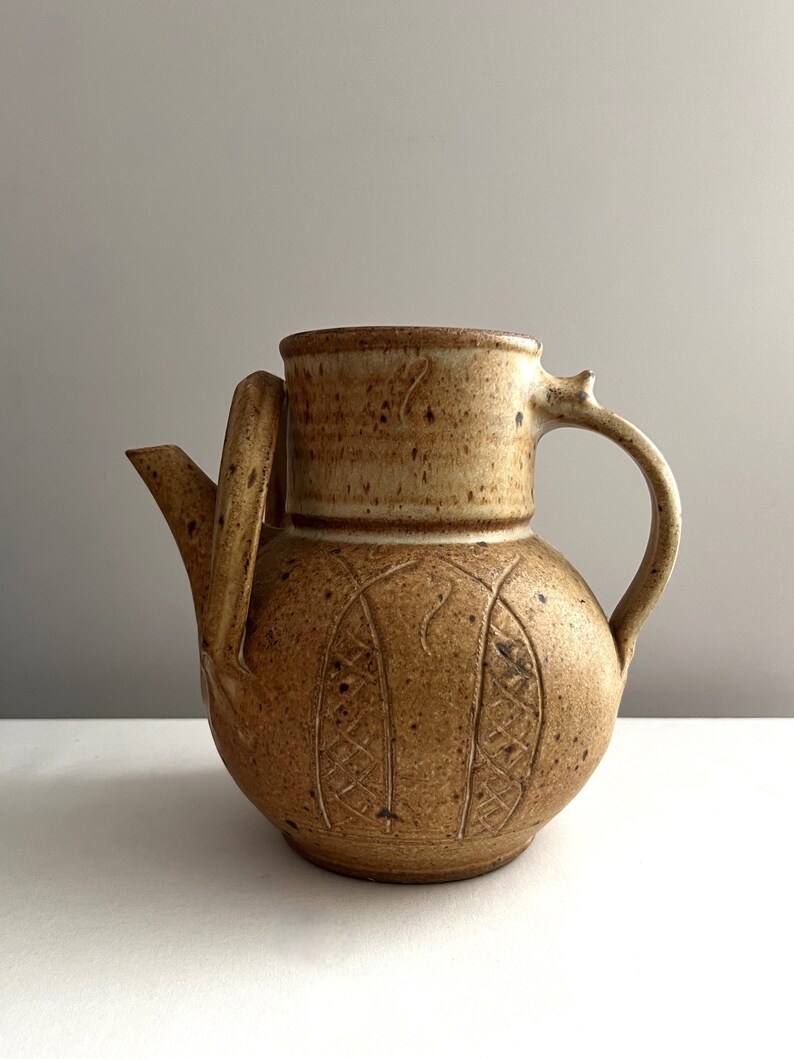 May include: A brown ceramic teapot with a textured surface and a carved design. The teapot has a handle and a spout.